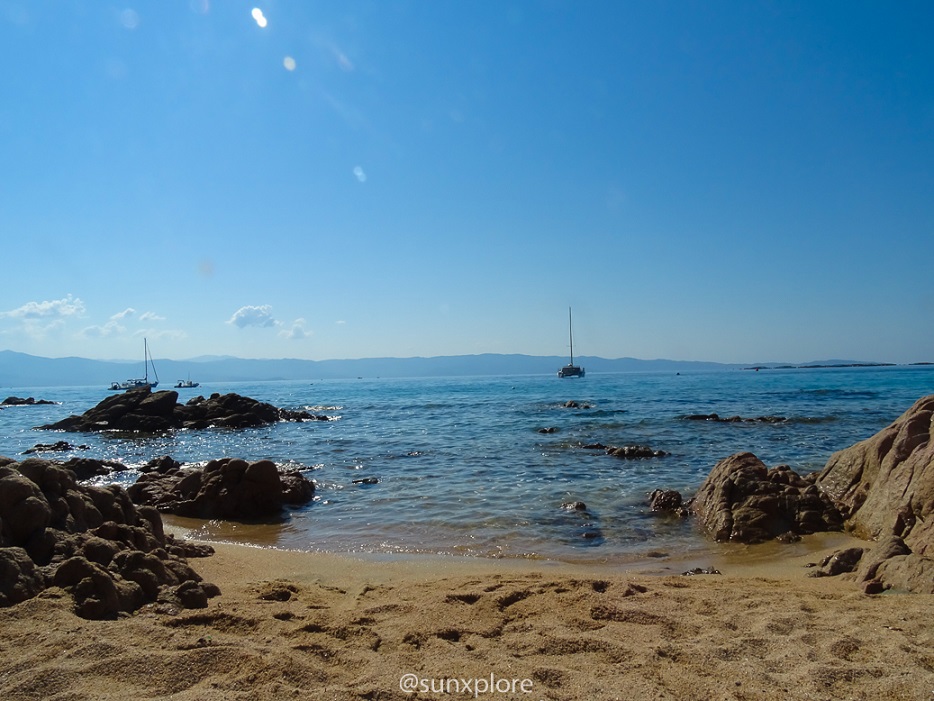 Entre le sable et les rochers, au milieu de l’eau turquoise d’une des plus belles plages de Corse, un voilier en mouillage profite de son après-midi 