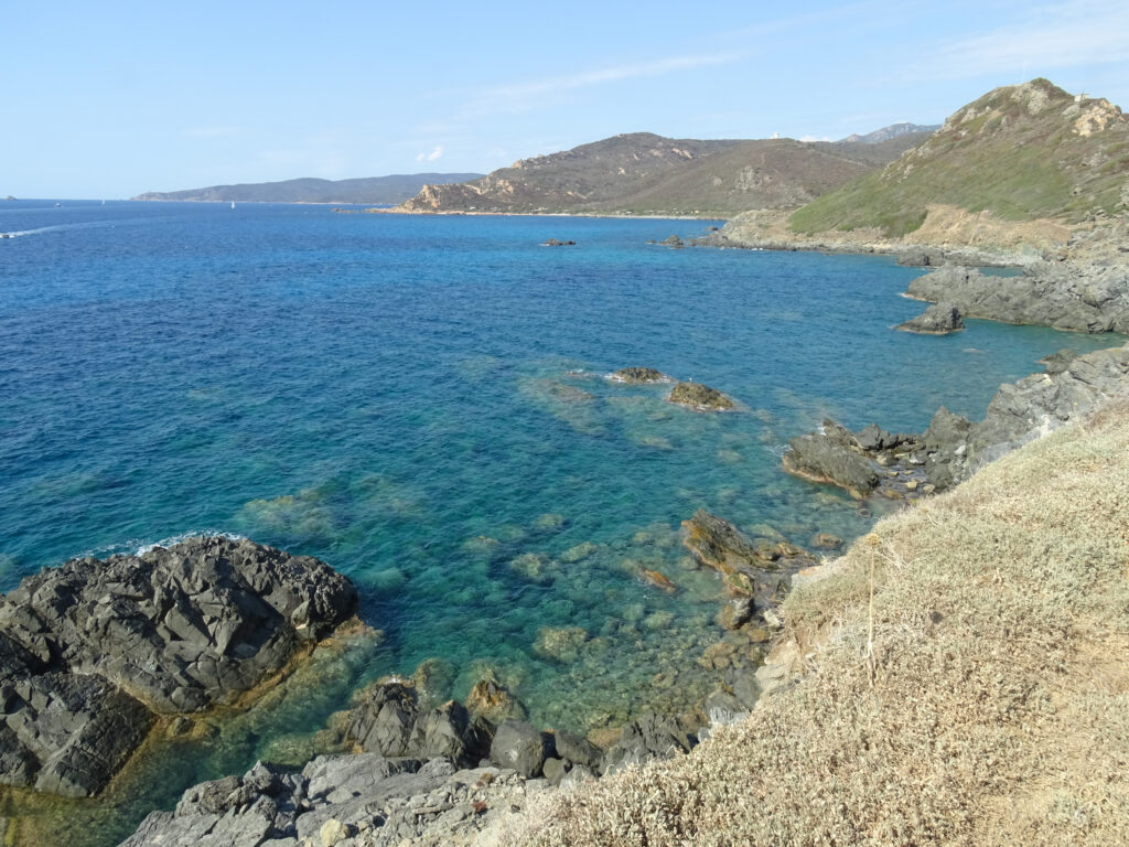Une photo qui montre le bord de mer à la presqu'île du Parata, avec des rochers, une eau turquoise et des collines en arrière-plan