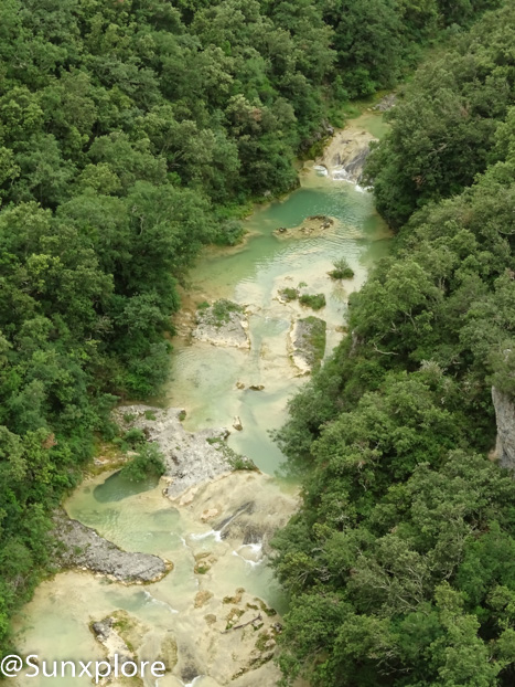 Une photo aérienne montrant les concluses de Lussan, des gorges creusées par une rivière dans le calcaire, avec des falaises blanches et des arbres verts.