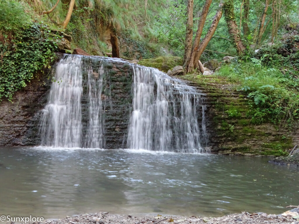 Cascade large et basse tombant sur des rochers au milieu de la forêt.