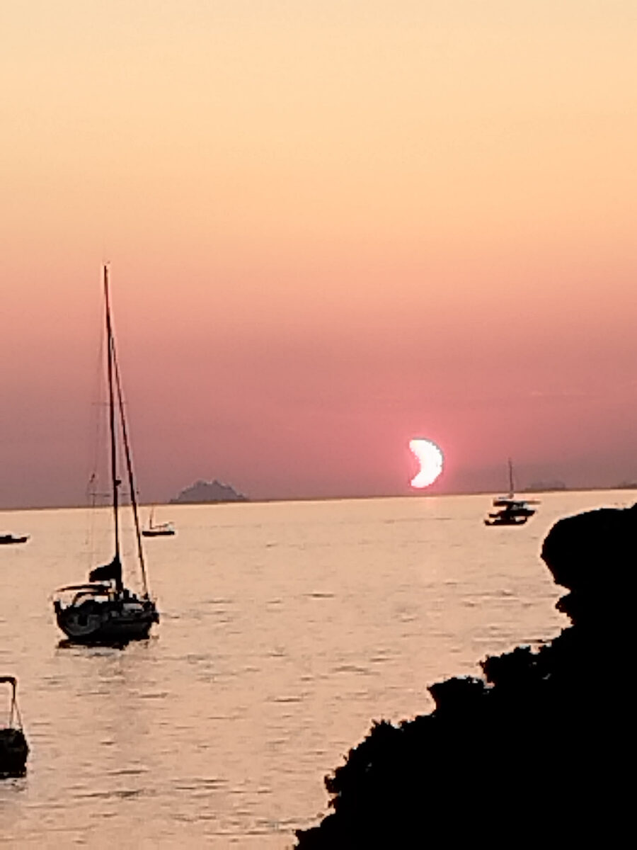 Croissant de Soleil éclipsé rose au-dessus de la mer avec un voilier au mouillage devant l'île des Embiez