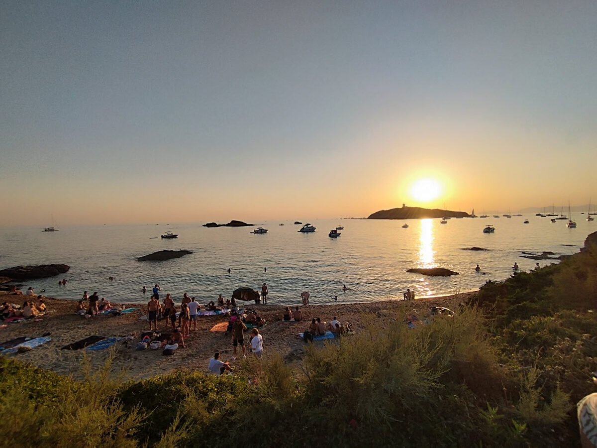 Plage de l'île des Embiez fréquentée en fin de journée, avec le Soleil bas au-dessus des bateaux au mouillage
