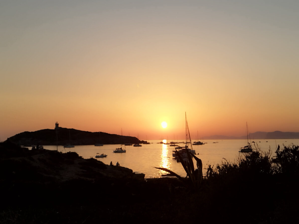 Soleil éclipsé touchant la mer derrière la silhouette de l'île des Embiez, avec un voilier au premier plan